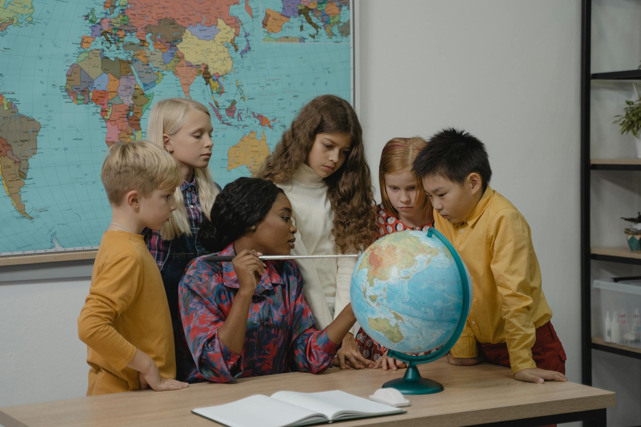A diverse group of children learning geography with a teacher and globe in a classroom.